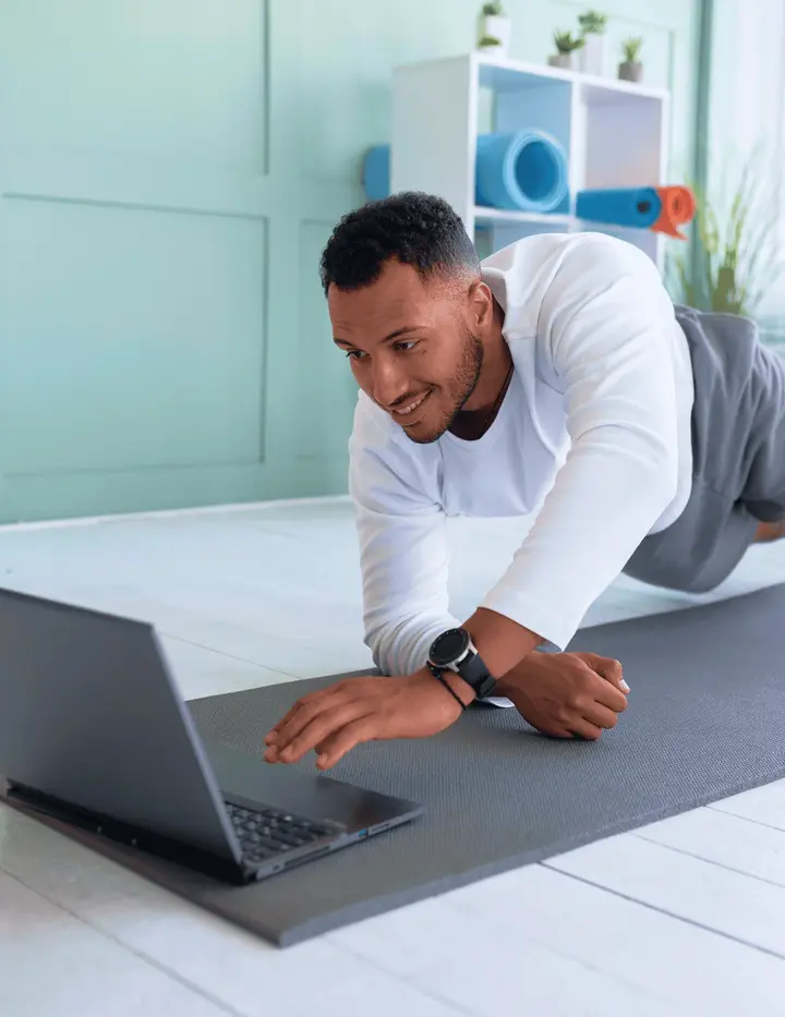 Man on a yoga mat using a laptop
