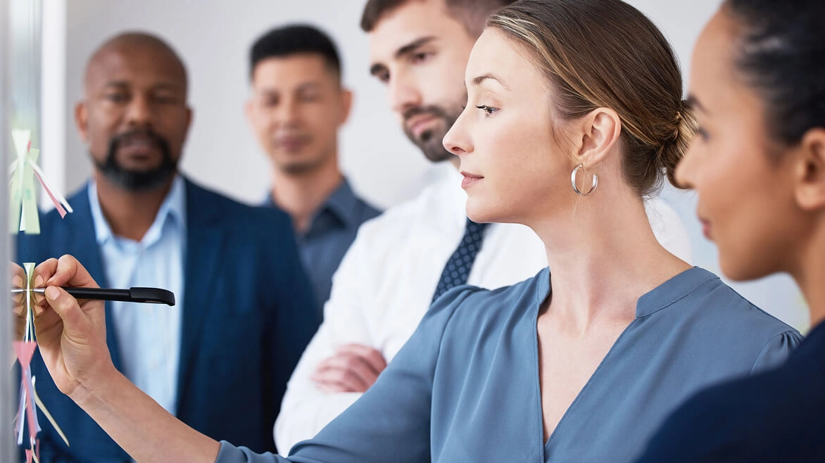 Photo of woman writing on a whiteboard surrounded by colleagues