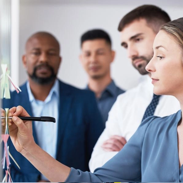 Photo of woman writing on a whiteboard surrounded by colleagues